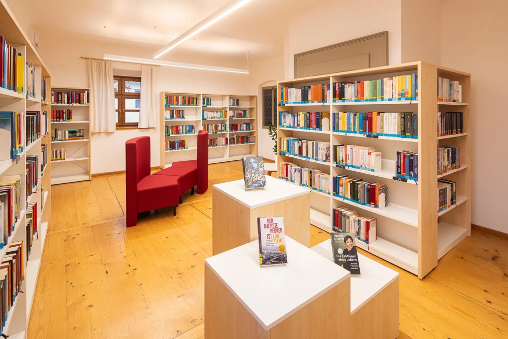 Innenraum der Bücherei Untermeitingen, mit Bücherregalen und einer roten Sitzgruppe